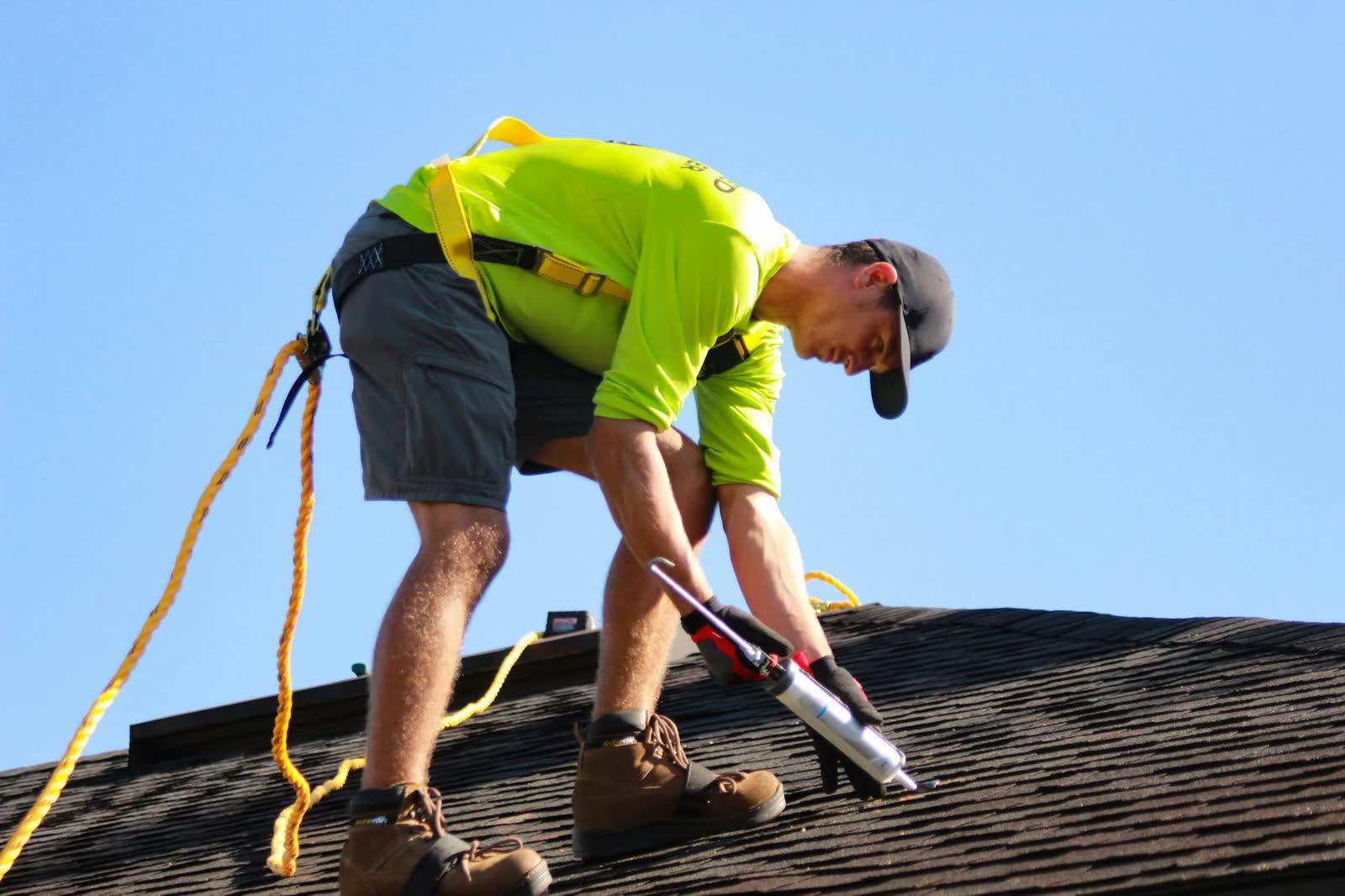 Roofer in a safety harness working on an asphalt shingle roof