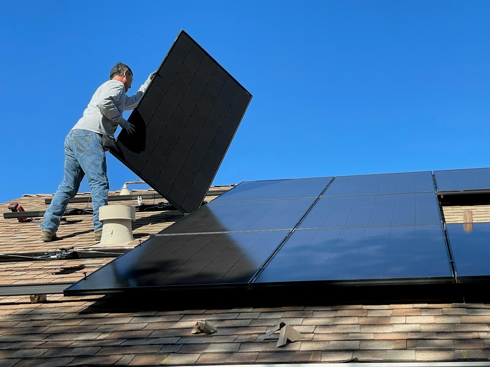 Installer placing a solar panel on a shingled roof