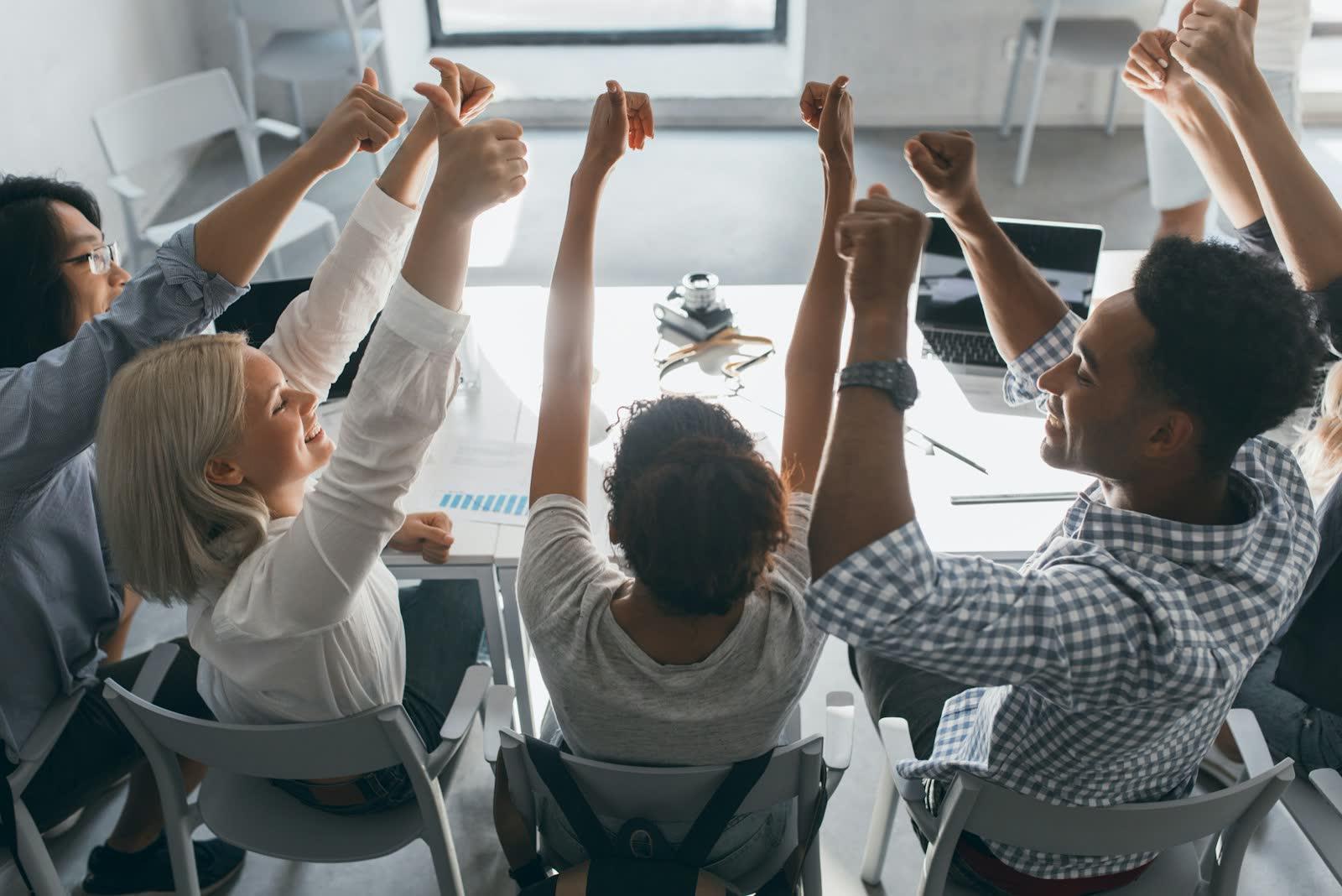 Sales team celebrating with their hands raised around a table